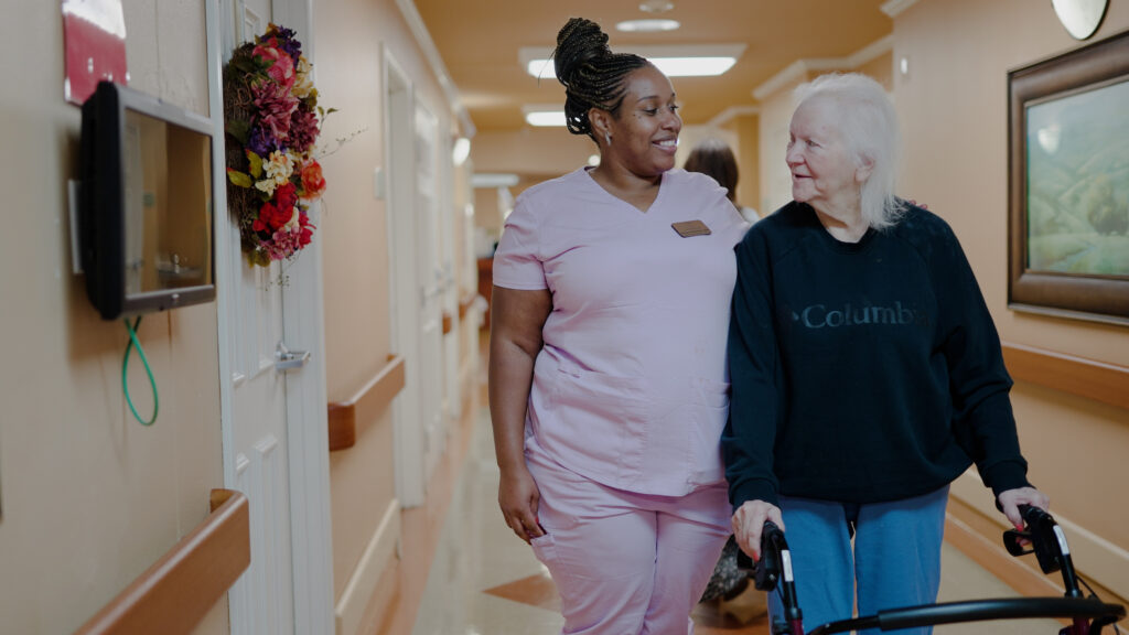 A woman and nurse smiling and walking down the hallway of a respite care facility